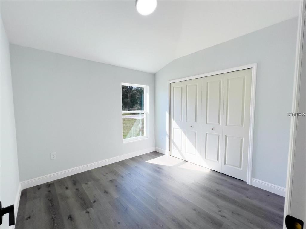 A bedroom features light gray walls, dark wood-look flooring, a window, and white closet doors — 3633 SE 138TH PLACE, SUMMERFIELD, FL