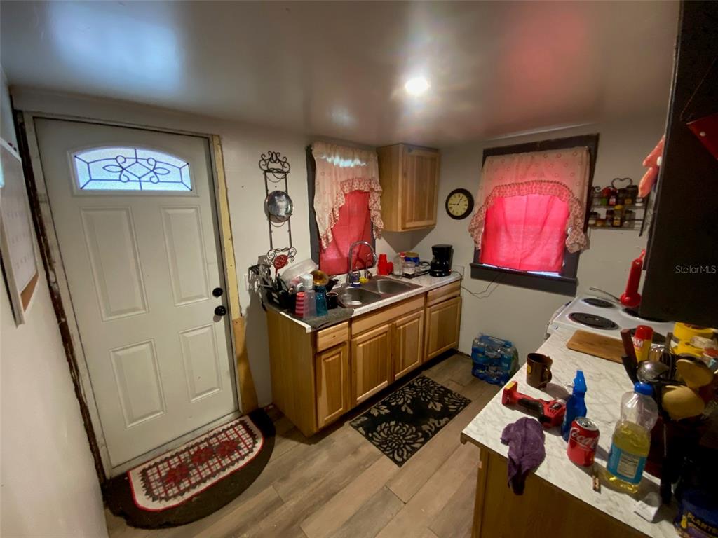 A kitchen features wood cabinets, a double sink, a white door, and red window curtains — 2714 SE 35TH STREET, GAINESVILLE, FL
