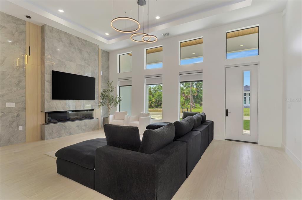 A modern living room features a large gray sectional, marble fireplace wall, and tall windows — 3708 MARSHALL ROAD, NORTH PORT, FL