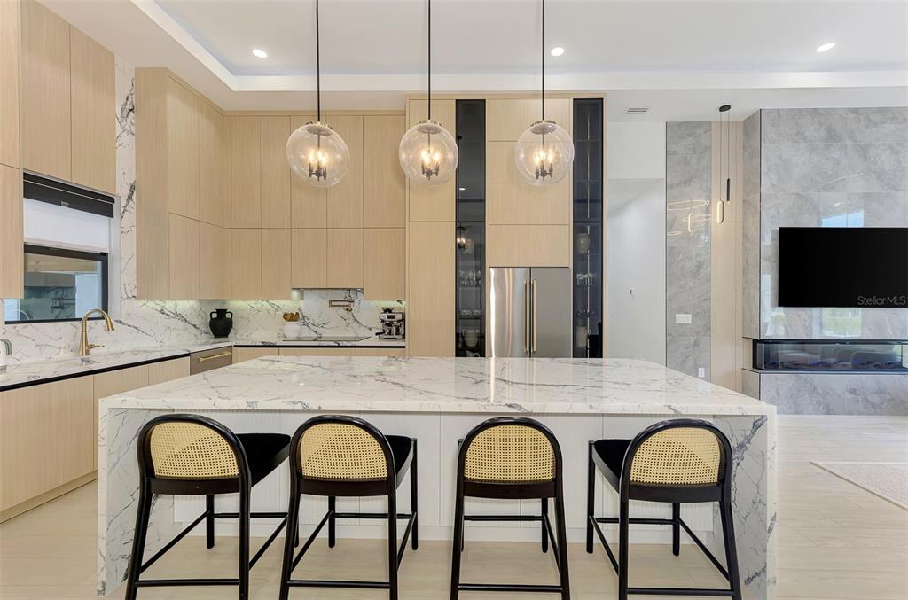 A modern kitchen features light wood cabinetry, a marble waterfall island, and four cane-backed stools — 3708 MARSHALL ROAD, NORTH PORT, FL