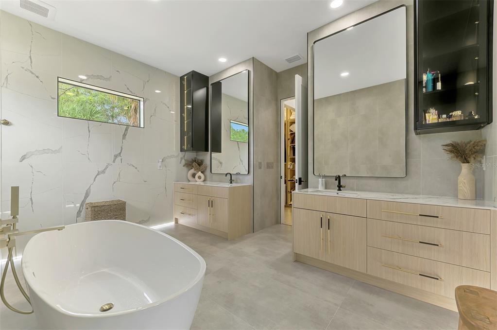 A modern bathroom features a freestanding tub, dual vanities, marble-look walls, and a walk-in closet — 3708 MARSHALL ROAD, NORTH PORT, FL