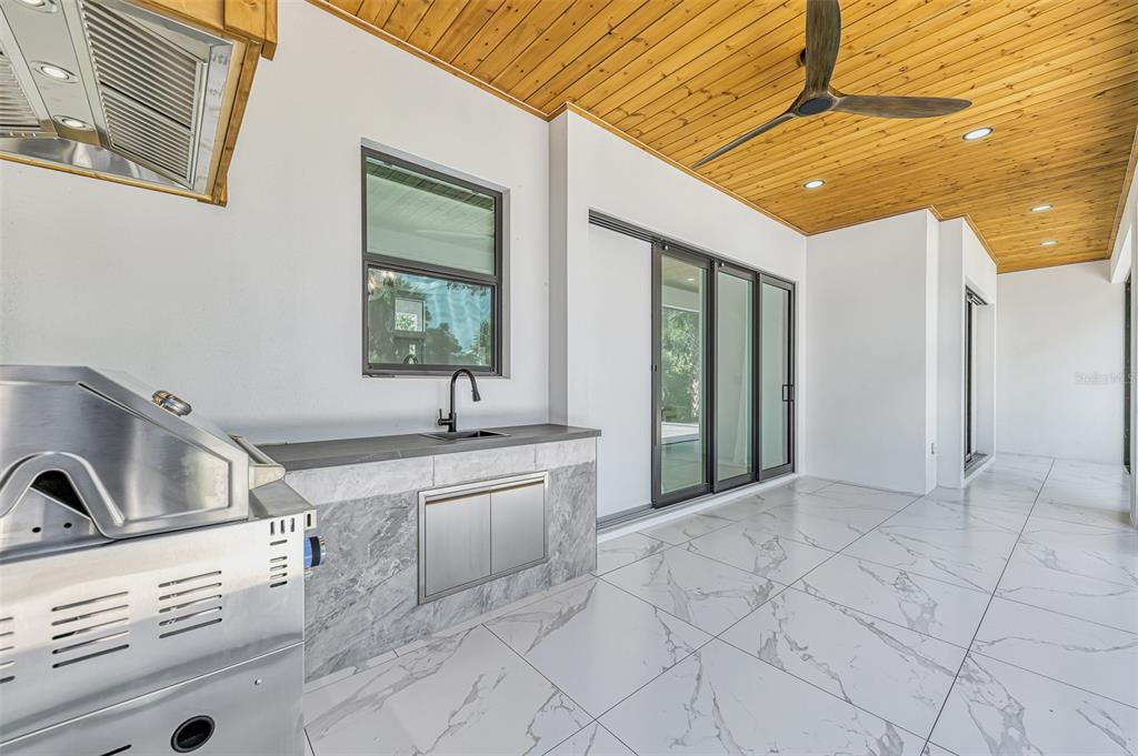 An outdoor kitchen with a grill, sink, and marble-look tile on a covered patio — 3708 MARSHALL ROAD, NORTH PORT, FL