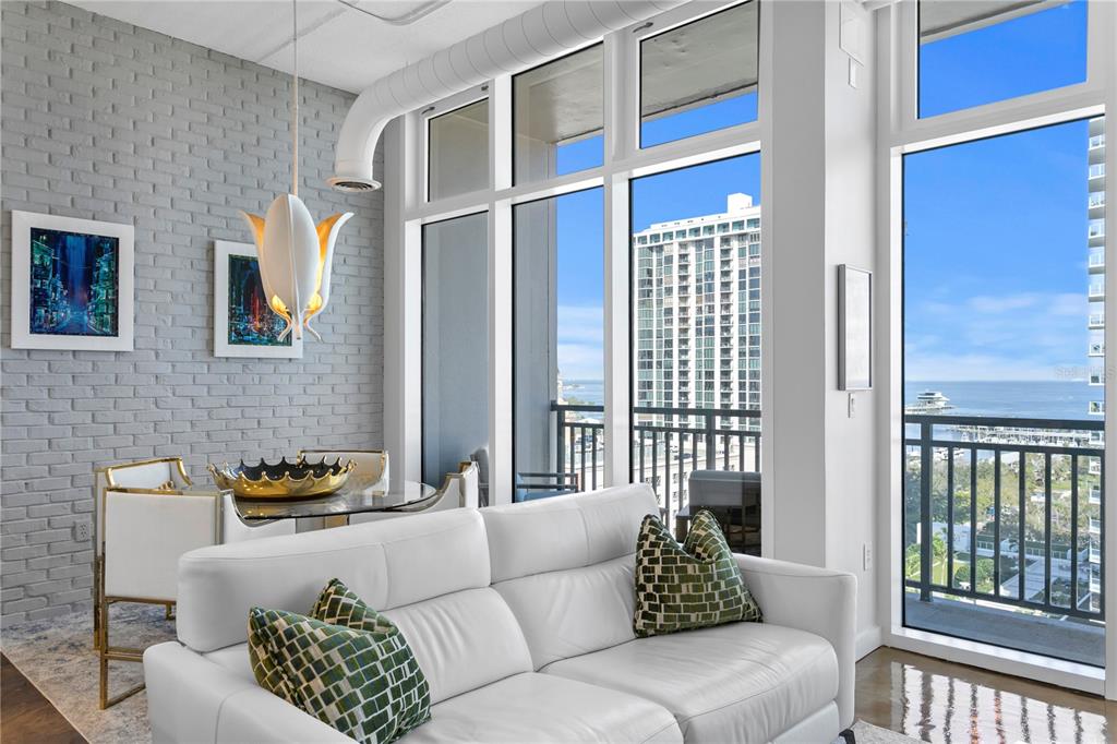 A living room with a white sofa, dining area, brick wall, and floor-to-ceiling windows — 175 2ND STREET S UNIT P-08, ST PETERSBURG, FL