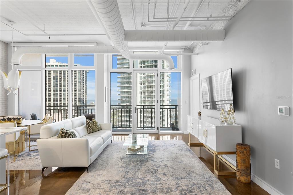 A modern living room features a white sofa, glass coffee table, and exposed ceiling ductwork — 175 2ND STREET S UNIT P-08, ST PETERSBURG, FL