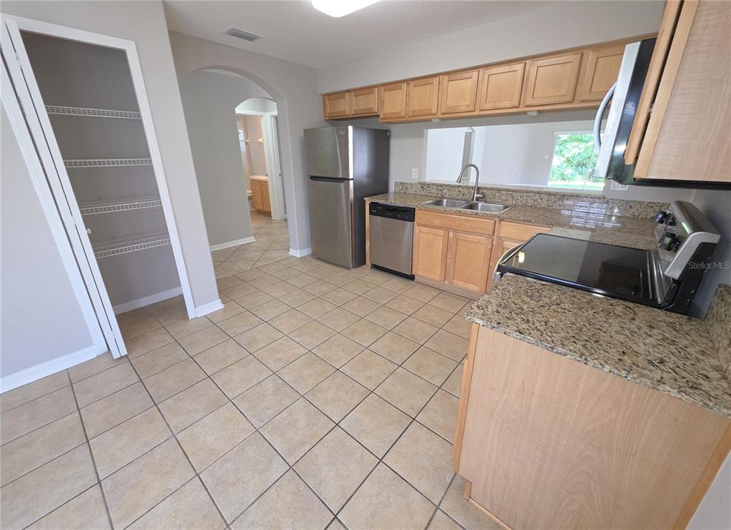 A kitchen features light wood cabinets, granite countertops, stainless steel appliances, and beige tile flooring — 25846 TERRAWOOD LOOP, LAND O LAKES, FL