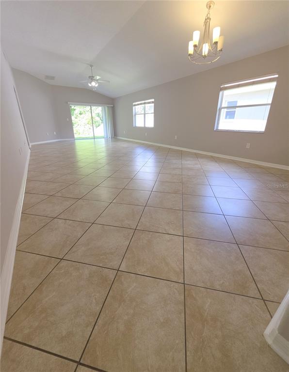 An empty room features large beige floor tiles, a vaulted ceiling, and a chandelier — 25846 TERRAWOOD LOOP, LAND O LAKES, FL