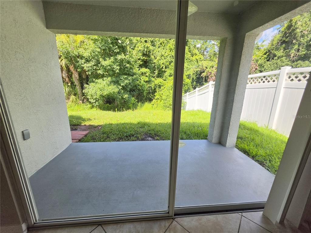 A covered concrete patio overlooks a grassy backyard enclosed by a white vinyl fence — 25846 TERRAWOOD LOOP, LAND O LAKES, FL