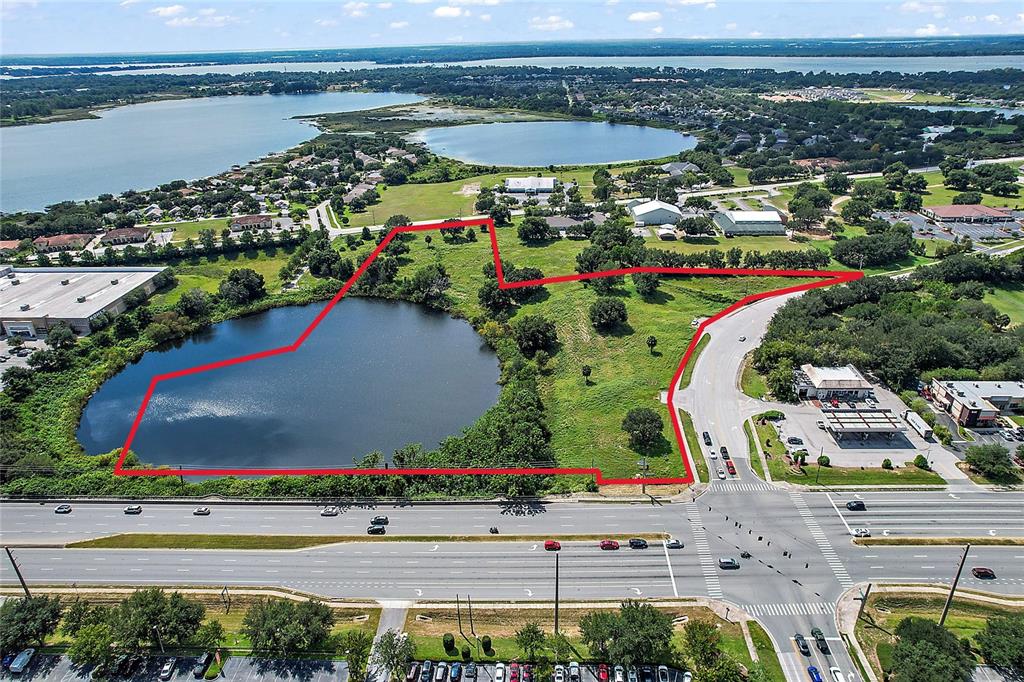 An aerial view shows a vacant, grassy lot featuring a large pond and road access — DAVID WALKER & US HWY 441 DRIVE, TAVARES, FL