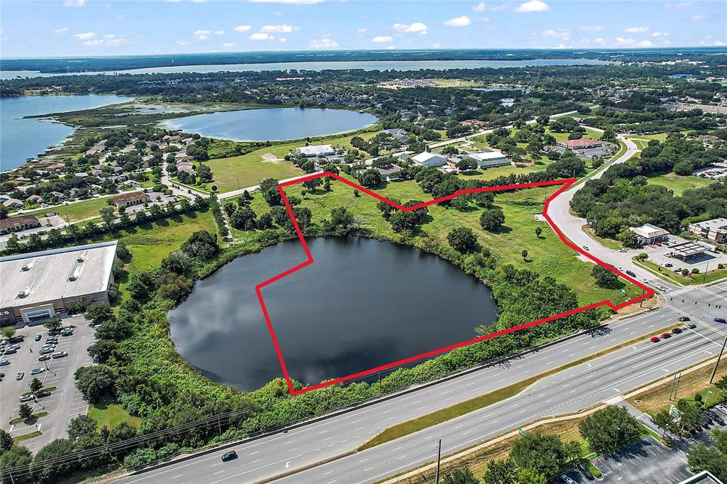 An aerial view shows a vacant, grassy lot surrounding a pond next to a highway — DAVID WALKER & US HWY 441 DRIVE, TAVARES, FL