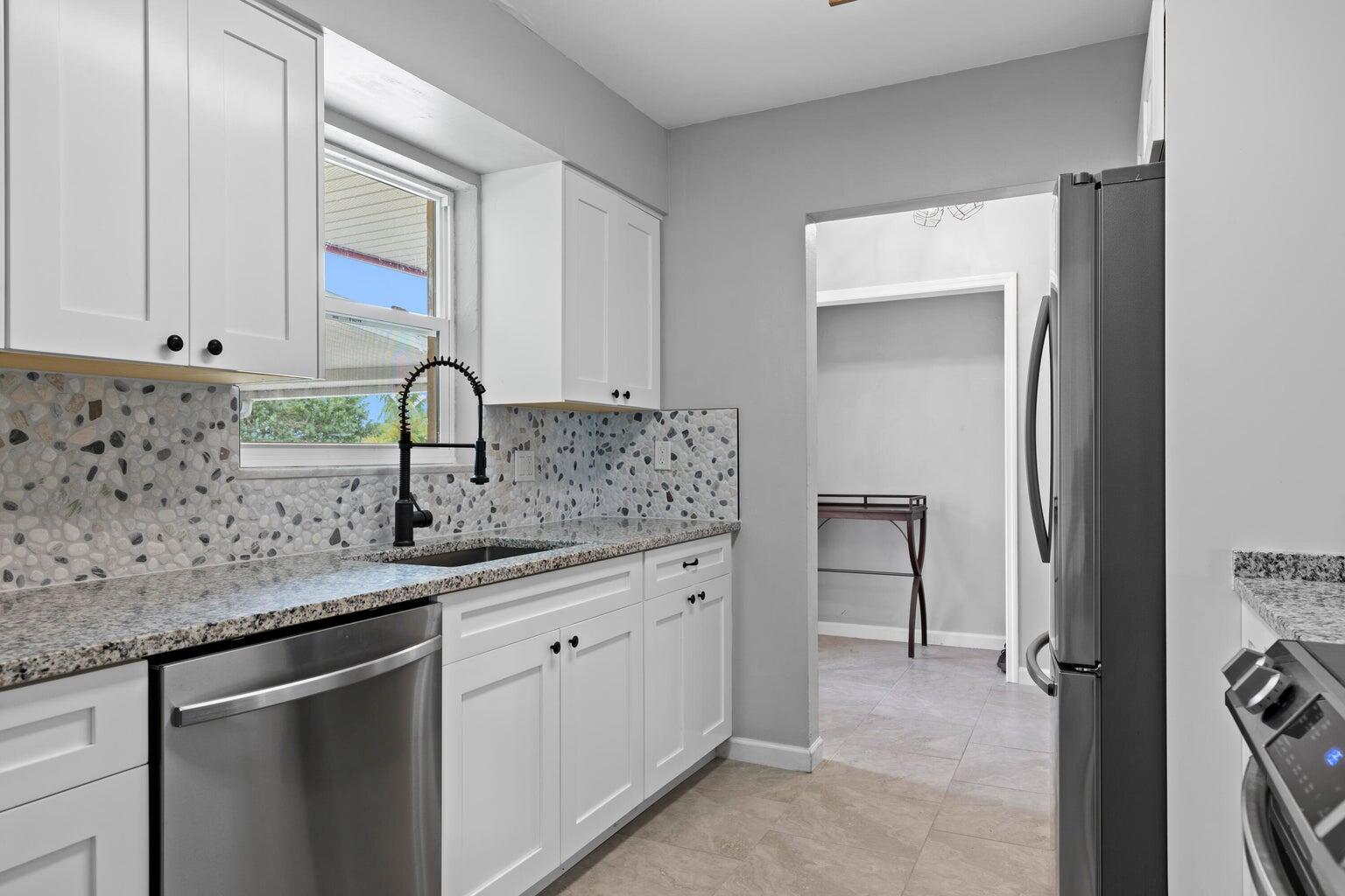 A kitchen features white cabinets, granite countertops, a pebble-tile backsplash, and stainless steel appliances — 474 22nd Street SE, Vero Beach FL 32962, VERO BEACH, FL