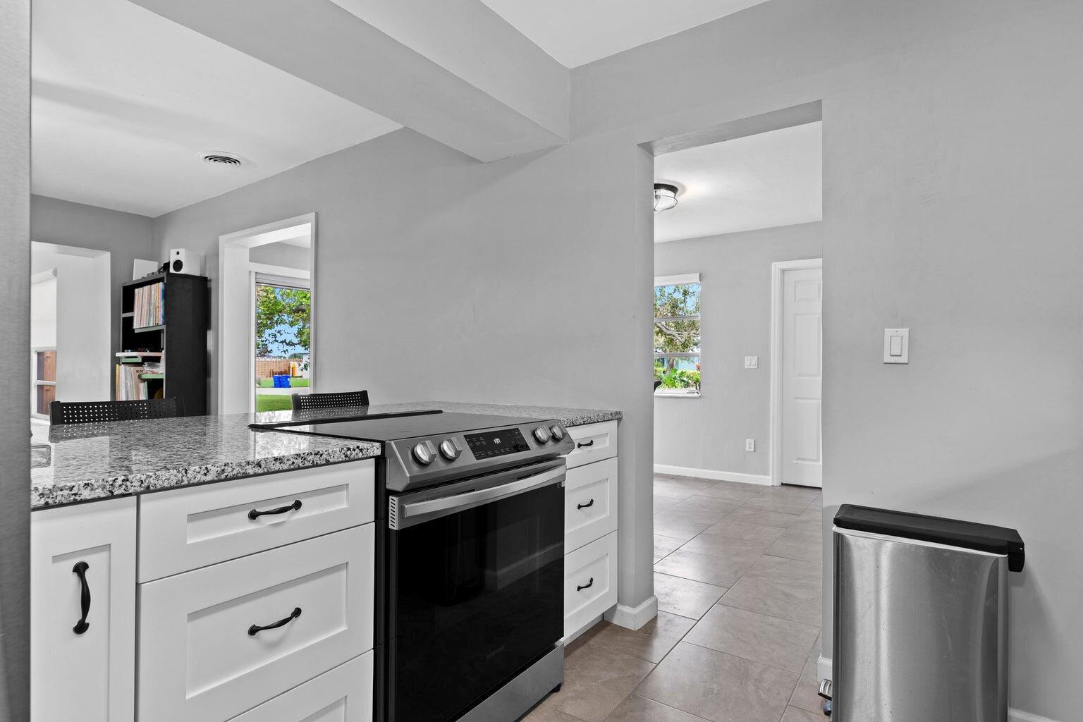 A kitchen features white cabinets, granite countertops, a stainless steel stove, and tile flooring — 474 22nd Street SE, Vero Beach FL 32962, VERO BEACH, FL