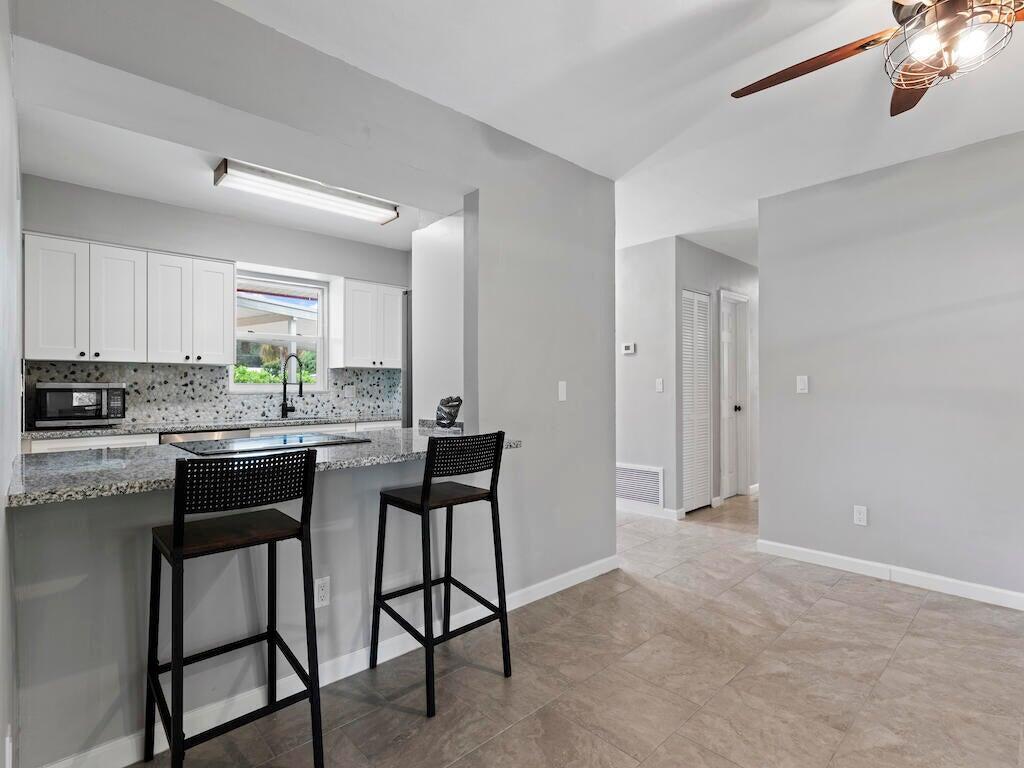 A kitchen with white cabinets, granite countertops, and a breakfast bar with two stools — 474 22nd Street SE, Vero Beach FL 32962, VERO BEACH, FL