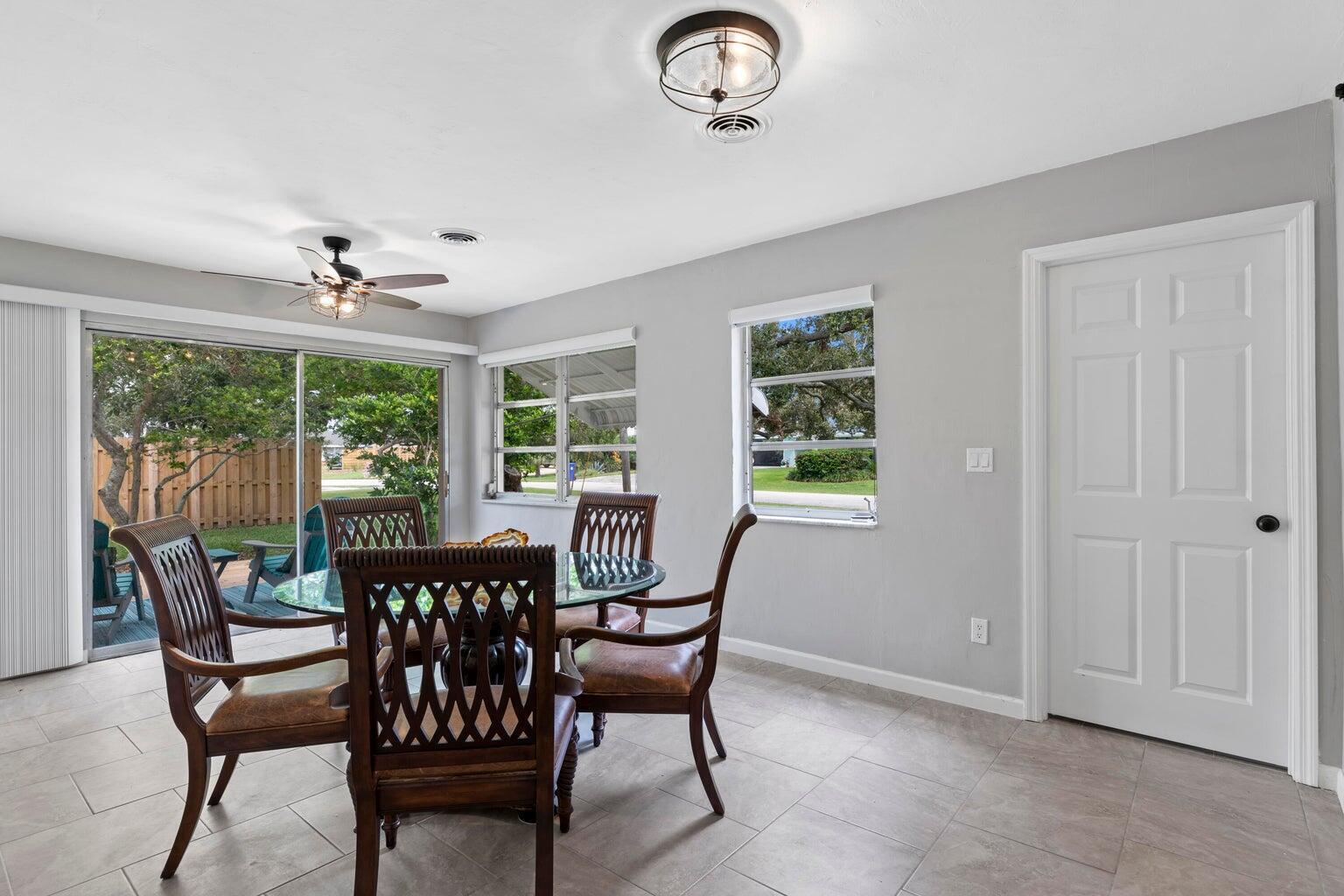 A dining area with a glass table, four wooden chairs, tile flooring, and sliding doors — 474 22nd Street SE, Vero Beach FL 32962, VERO BEACH, FL