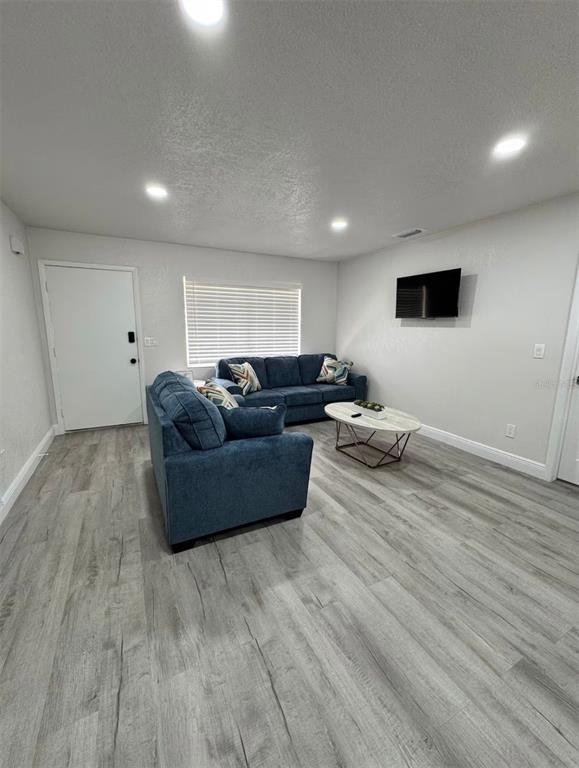 A living room features blue sofas, a coffee table, a wall-mounted television, and wood-look flooring — 5120 LANDOVER BOULEVARD, SPRING HILL, FL