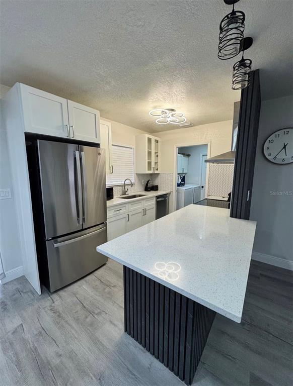 A modern kitchen features a white quartz island, stainless steel appliances, and wood-slat cabinetry — 5120 LANDOVER BOULEVARD, SPRING HILL, FL