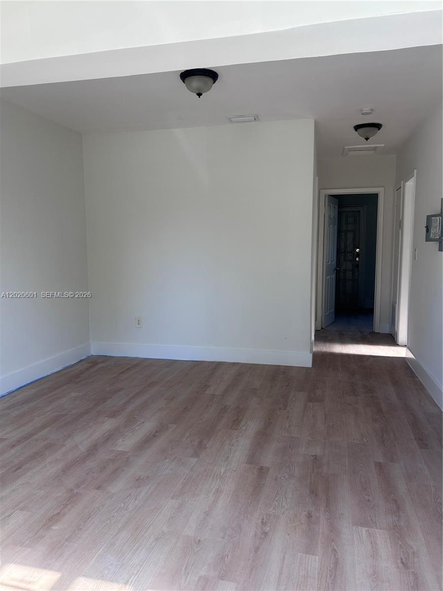 An empty room features light wood-look flooring, white walls, and two ceiling-mounted light fixtures — 1820 NW 73rd St, Miami FL 33147, MIAMI, FL
