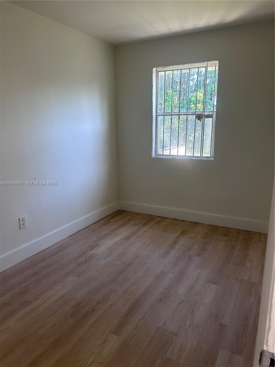This empty bedroom features light-colored wood-look flooring, plain walls, and a window with security bars — 1820 NW 73rd St, Miami FL 33147, MIAMI, FL