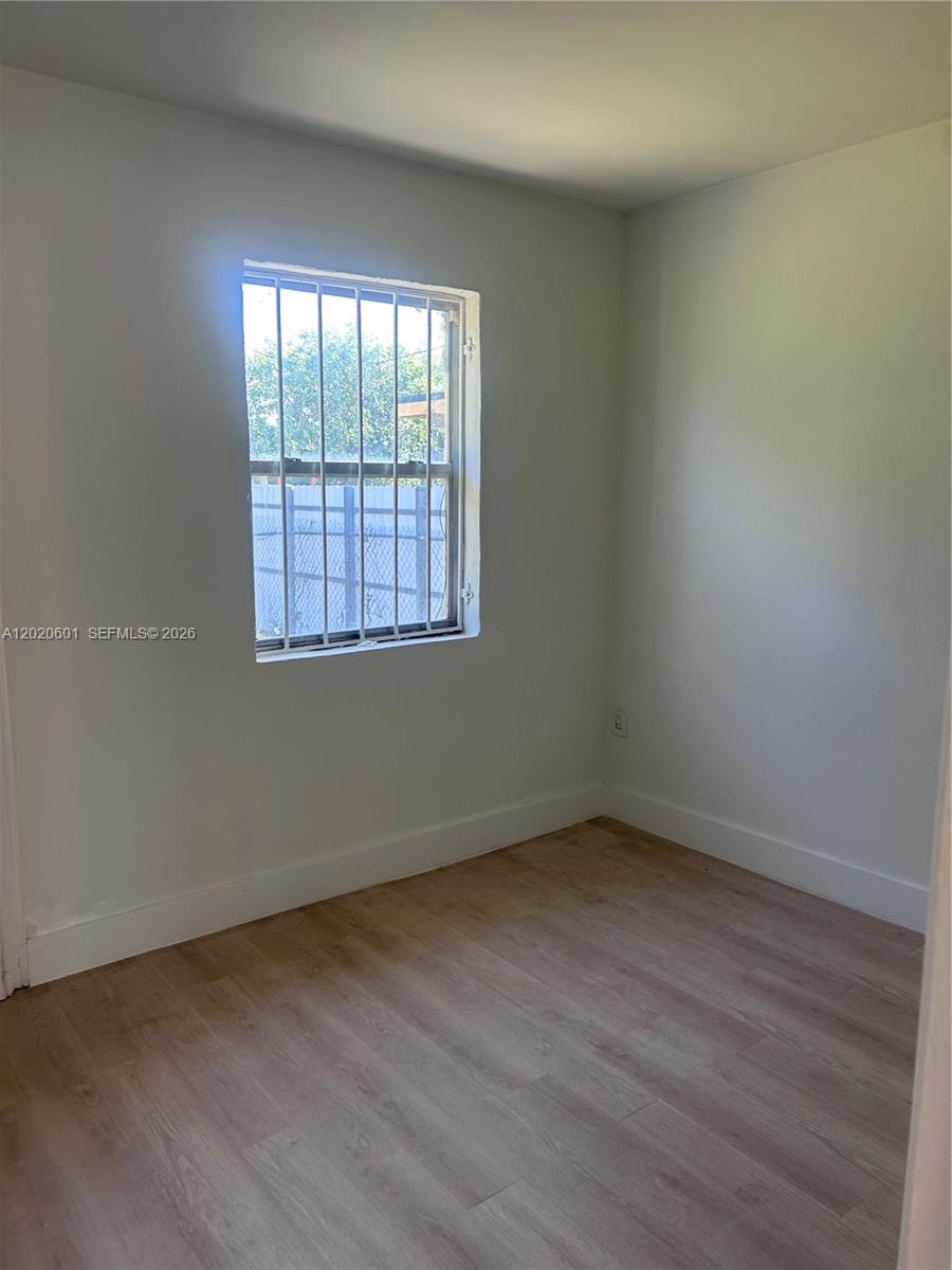 An empty room features light wood-look flooring, white walls, and a window with security bars — 1820 NW 73rd St, Miami FL 33147, MIAMI, FL
