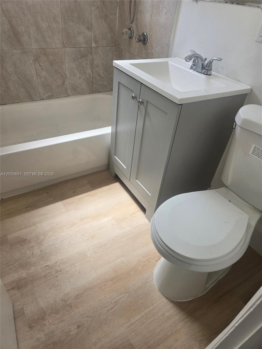 A small bathroom features a gray vanity, a white toilet, and a tiled bathtub surround — 1820 NW 73rd St, Miami FL 33147, MIAMI, FL
