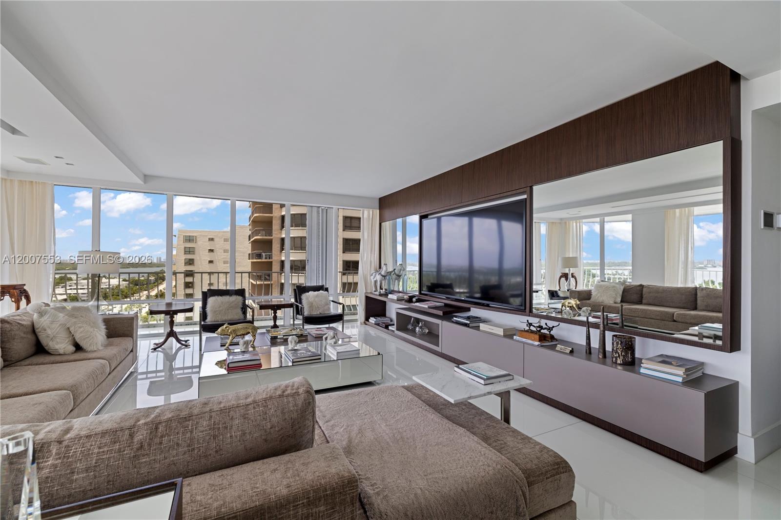 A modern living room features a large sectional sofa, a mirrored coffee table, and a media wall — 10155 Collins Ave # 1210, Bal Harbour FL 33154, BAL HARBOUR, FL