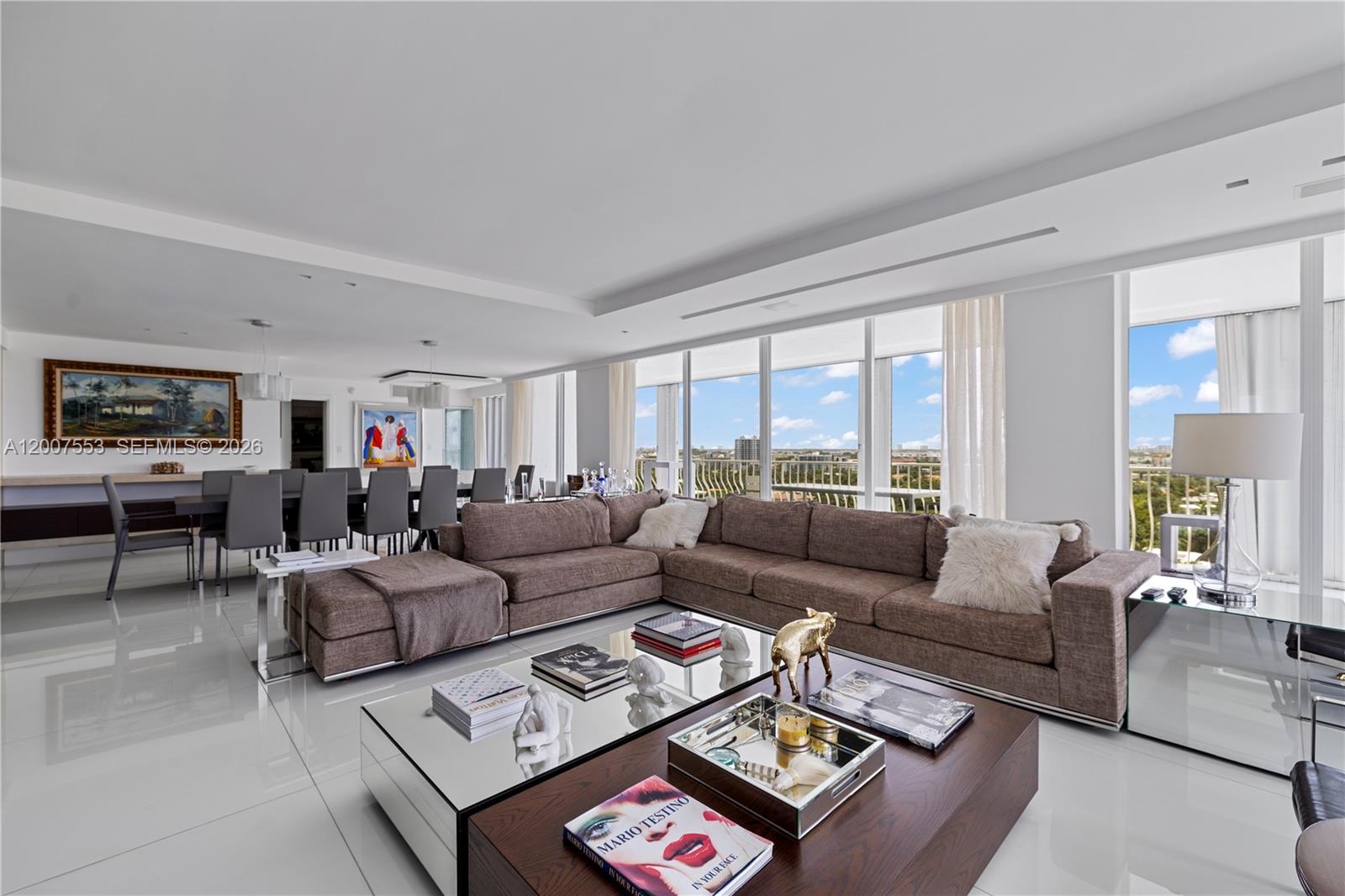 A modern living and dining area features a large sectional sofa, mirrored coffee table, and floor-to-ceiling windows — 10155 Collins Ave # 1210, Bal Harbour FL 33154, BAL HARBOUR, FL