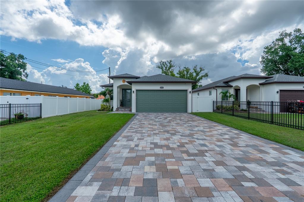 A single-story house with a green garage door and a paved driveway under a cloudy sky — 8307 N GOMEZ AVENUE, TAMPA, FL