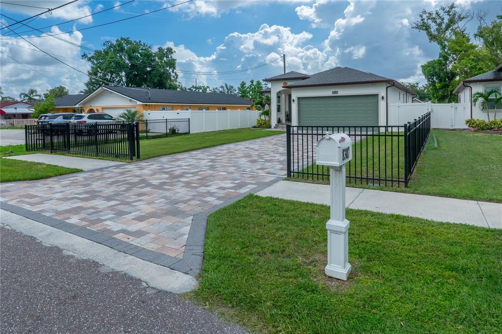 A paved driveway leads to a single-story house with a green garage door and fencing — 8307 N GOMEZ AVENUE, TAMPA, FL