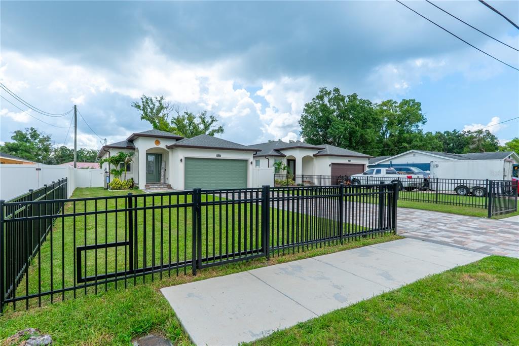 A single-story house with a green garage door and a black metal fence in front — 8307 N GOMEZ AVENUE, TAMPA, FL