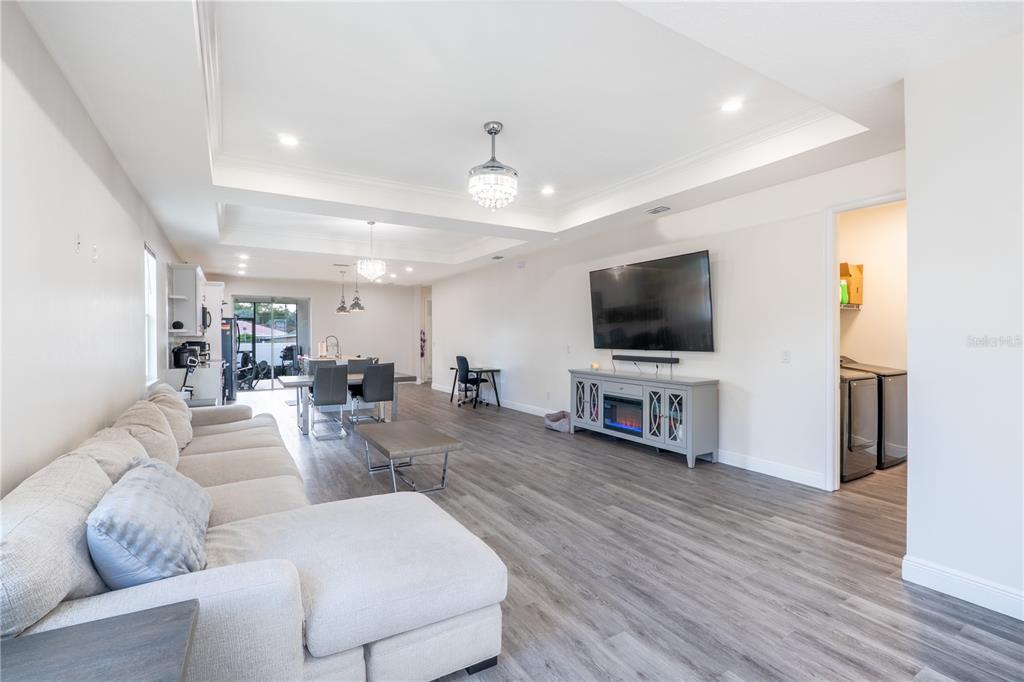 This open-concept living room features a sectional sofa, dining area, and a wall-mounted television — 8307 N GOMEZ AVENUE, TAMPA, FL