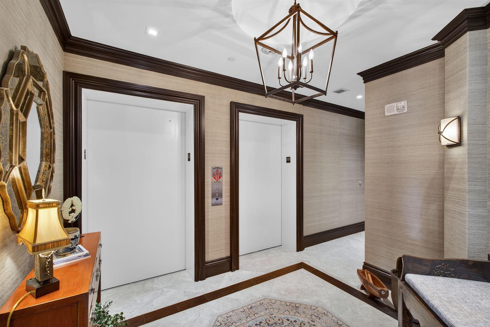 An elevator lobby features two white doors, textured wallpaper, dark wood trim, and a chandelier — 2700 N Ocean Drive # 1401a, Riviera Beach FL 33404, RIVIERA BEACH, FL