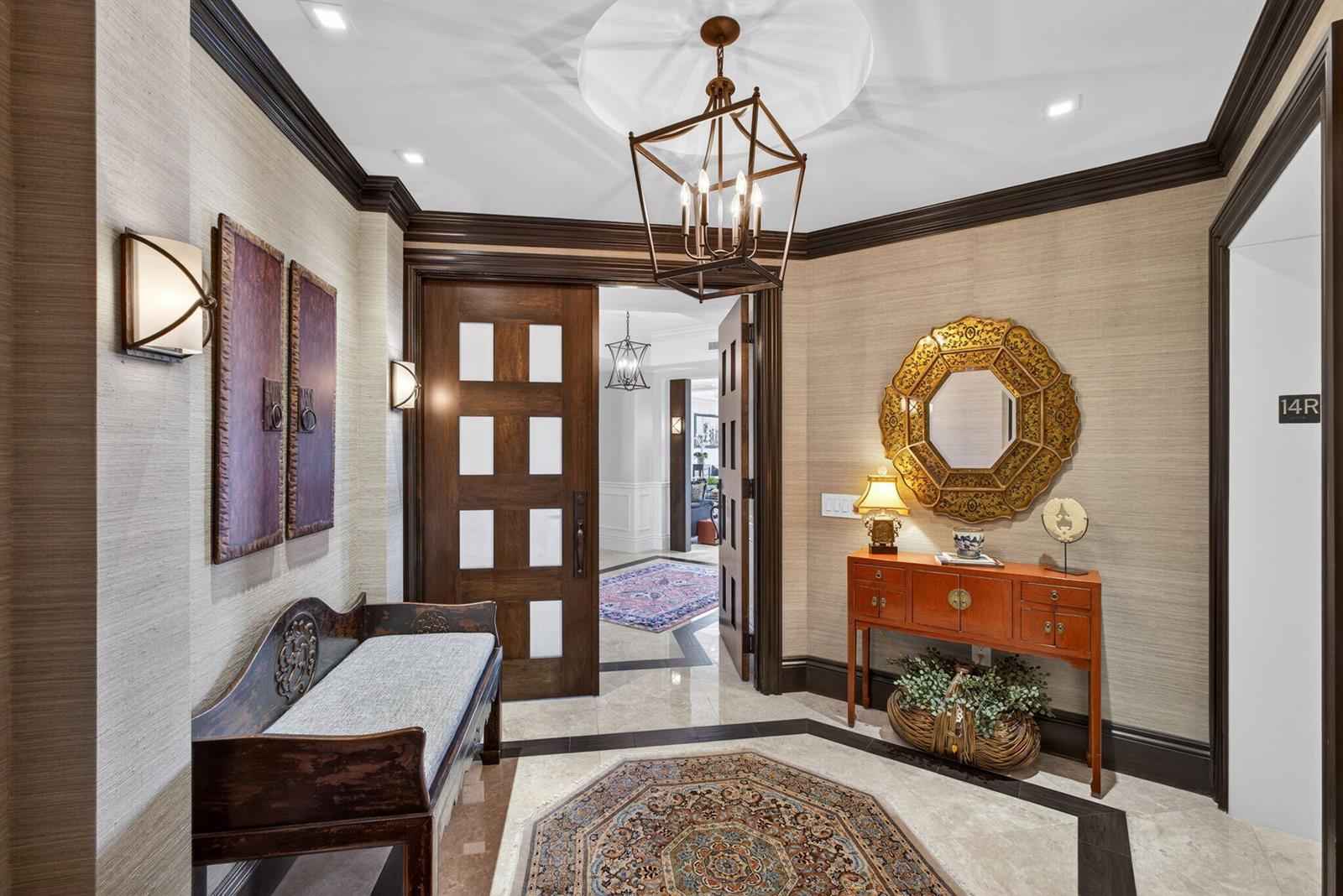 An elegant foyer features textured wallpaper, a geometric chandelier, a wooden bench, and a mirror — 2700 N Ocean Drive # 1401a, Riviera Beach FL 33404, RIVIERA BEACH, FL