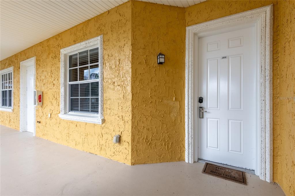 A yellow stucco exterior wall features two white doors, a window, and a doormat — 21012 PICASSO COURT UNIT 202, LAND O LAKES, FL