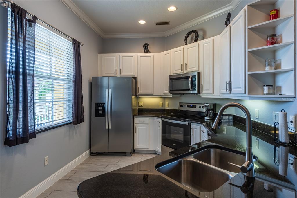 A kitchen features white cabinets, black granite countertops, stainless steel appliances, and a double sink — 21012 PICASSO COURT UNIT 202, LAND O LAKES, FL
