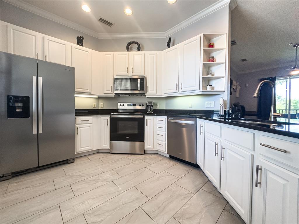 A kitchen features white cabinets, stainless steel appliances, black countertops, and light-colored tile flooring — 21012 PICASSO COURT UNIT 202, LAND O LAKES, FL