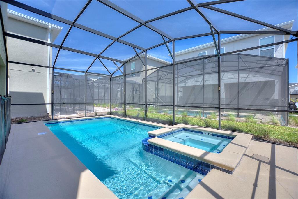 A screened-in swimming pool and spa with a concrete deck behind a residential home — 4285 PROLOGUE WAY, KISSIMMEE, FL