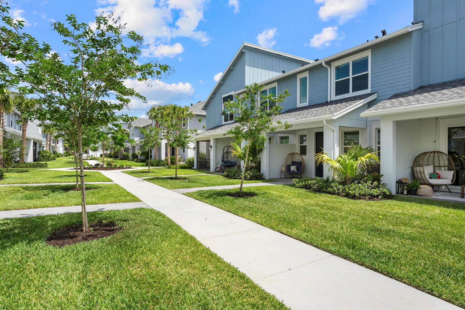 A row of blue two-story townhomes with front porches and green lawns under a blue sky — 16417 Mirabell Manor Lane, FL 33470, FL