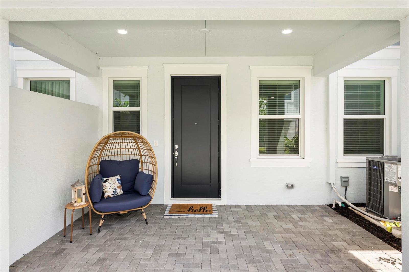 A covered patio features a black front door, a wicker egg chair, and paver flooring — 16417 Mirabell Manor Lane, FL 33470, FL