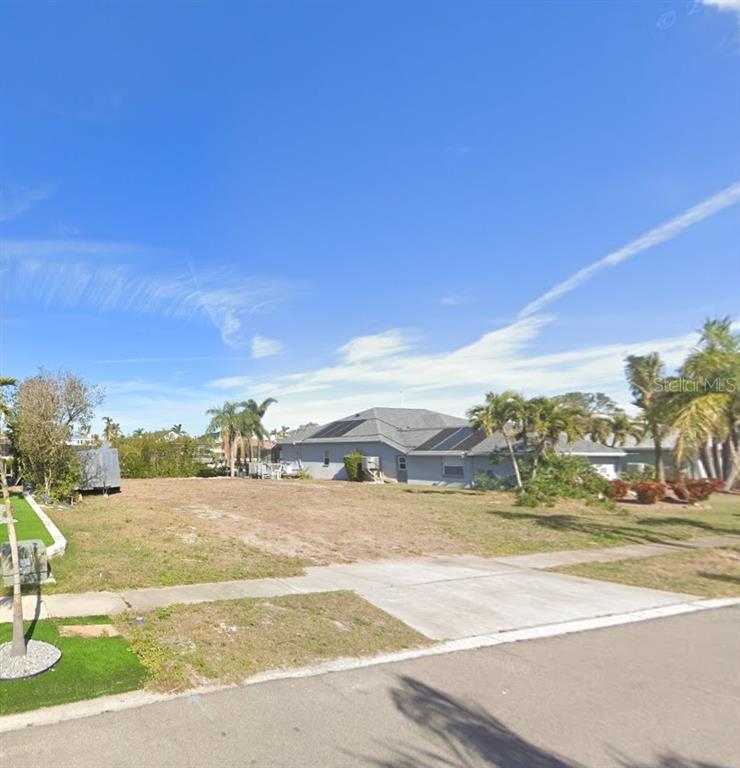 A vacant, grassy residential lot sits in front of a single-story house with solar panels — 6508 BLACKFIN WAY, APOLLO BEACH, FL