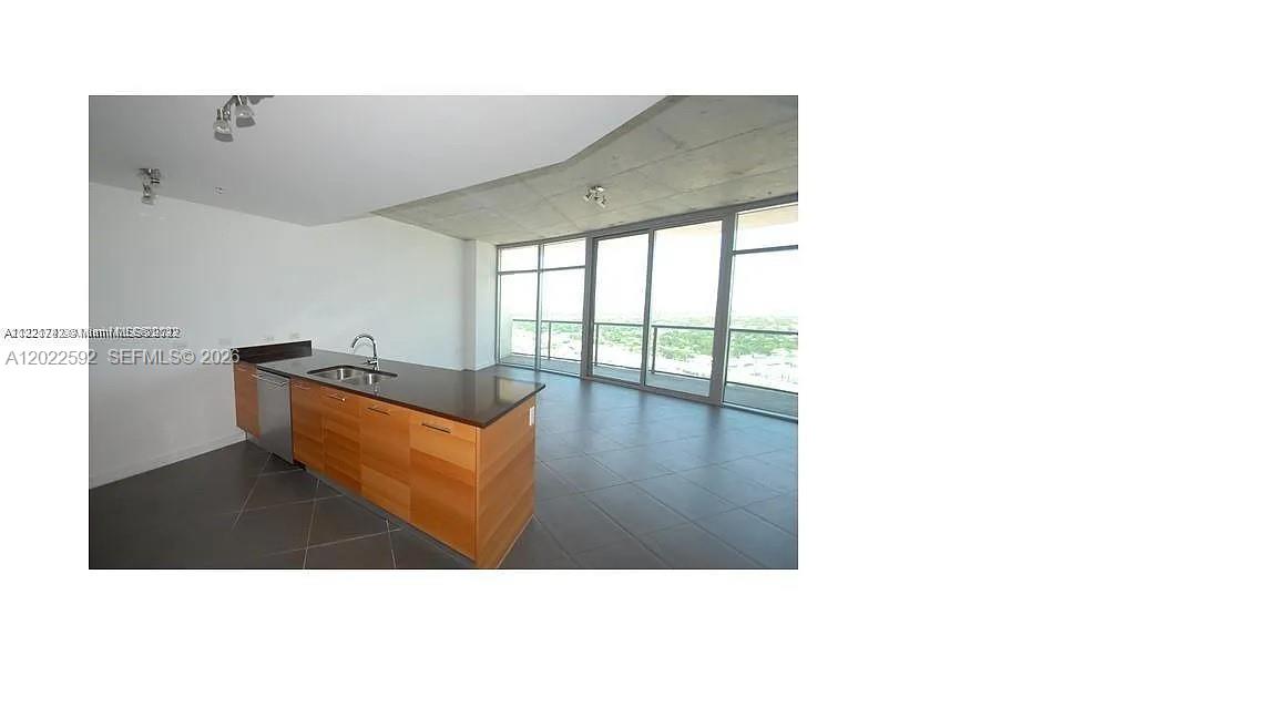 A modern kitchen with wood cabinets and a dark countertop overlooks an open living area — 3301 NE 1st Ave # H2709, Miami FL 33137, MIAMI, FL
