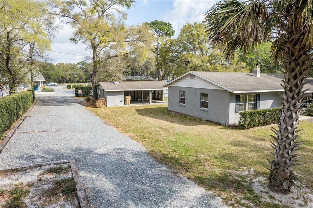 A gravel driveway leads toward a gray house and a detached carport on a grassy lot — 25525 COLMAR AVENUE, SORRENTO, FL