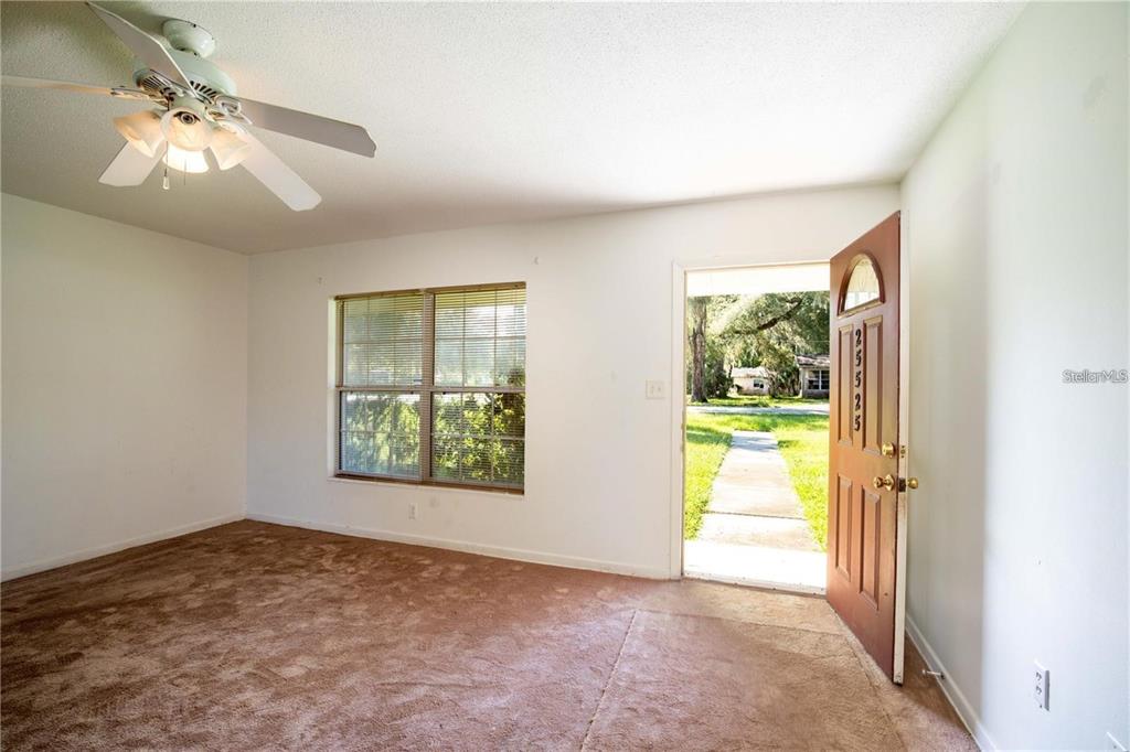 A carpeted room features a ceiling fan, a large window, and an open front door — 25525 COLMAR AVENUE, SORRENTO, FL