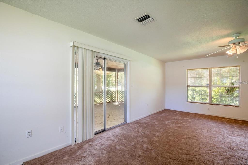 A carpeted living room features a sliding glass door, a ceiling fan, and a window — 25525 COLMAR AVENUE, SORRENTO, FL