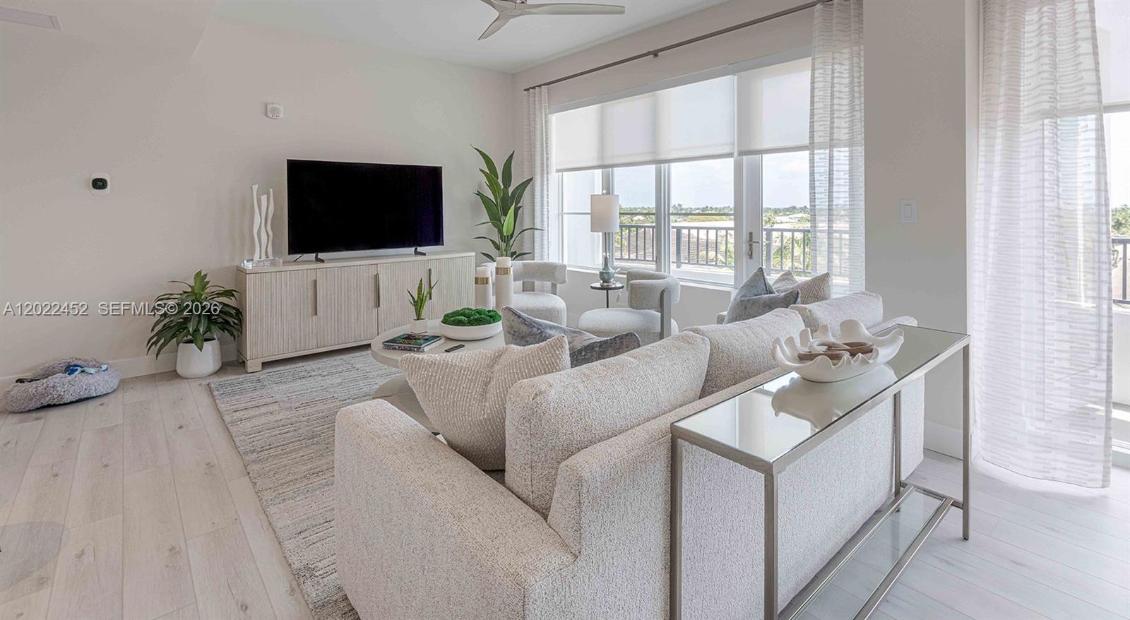 A bright living room features a light-colored sofa, a television console, and large windows — 151 NE 5th Ave, Delray Beach FL 33483, DELRAY BEACH, FL