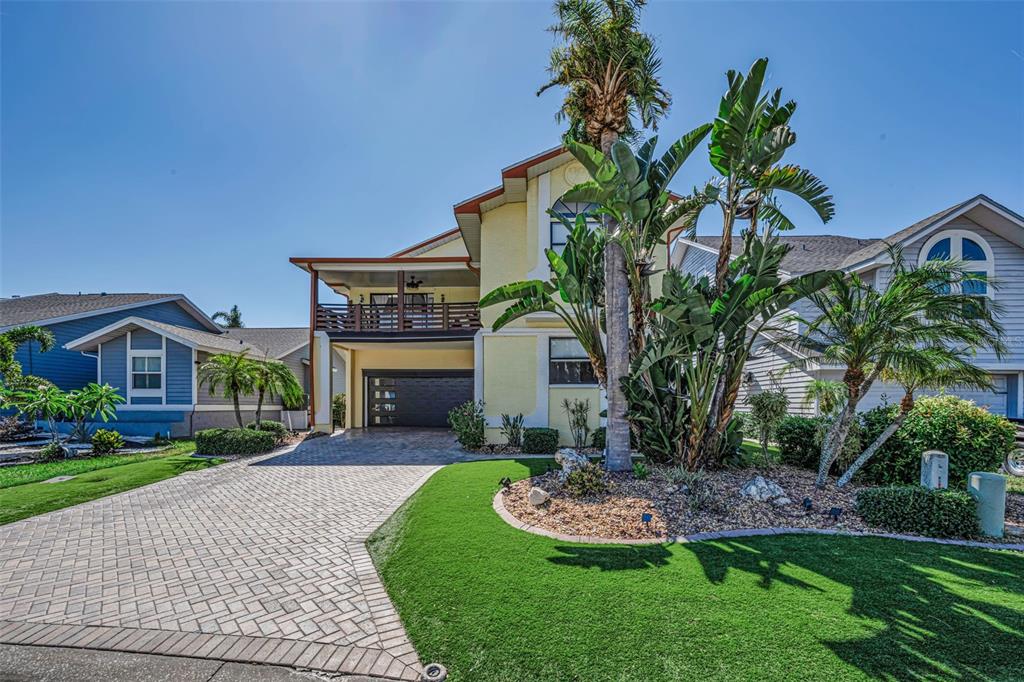 A yellow two-story house with a paved driveway, a balcony, and a landscaped front yard — 6009 BAYWAY COURT, NEW PORT RICHEY, FL