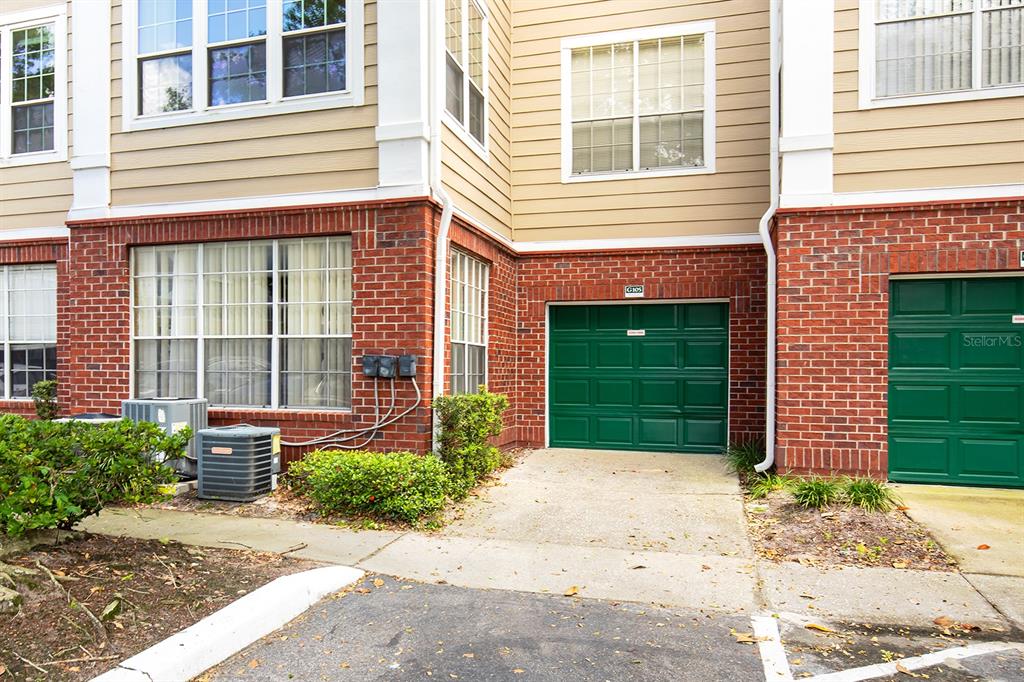 An exterior view of a multi-story building with two green garage doors and brick siding — 13015 PLANTATION PARK CIRCLE UNIT 1027, ORLANDO, FL