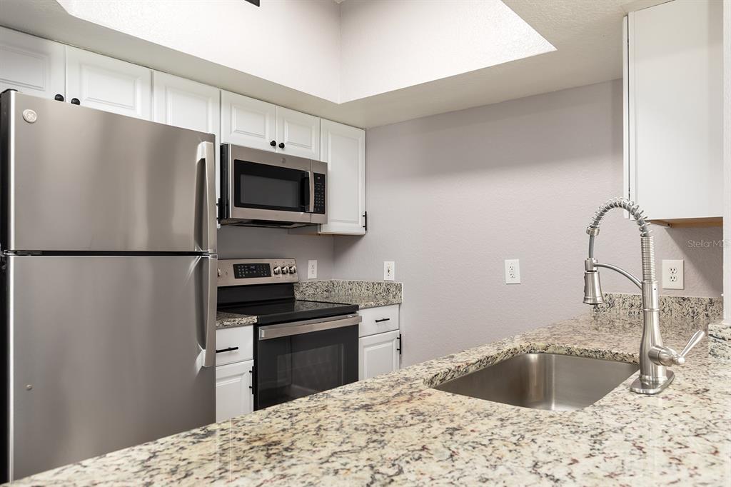 A kitchen features stainless steel appliances, white cabinets, and granite countertops with a sink — 13015 PLANTATION PARK CIRCLE UNIT 1027, ORLANDO, FL