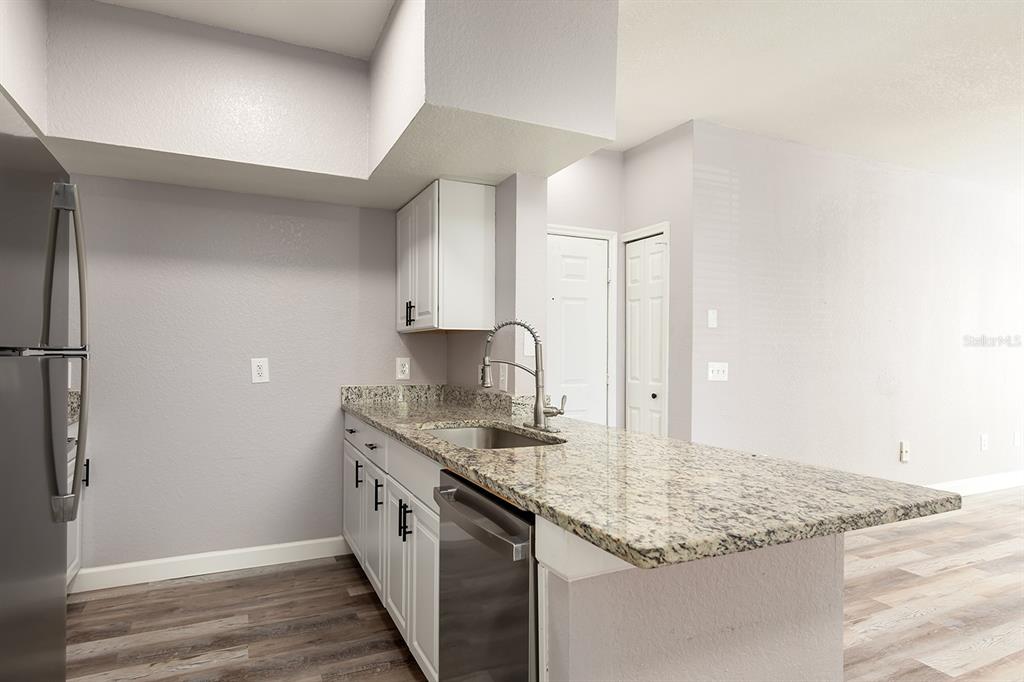 A kitchen features white cabinets, granite countertops, stainless steel appliances, and wood-look flooring — 13015 PLANTATION PARK CIRCLE UNIT 1027, ORLANDO, FL