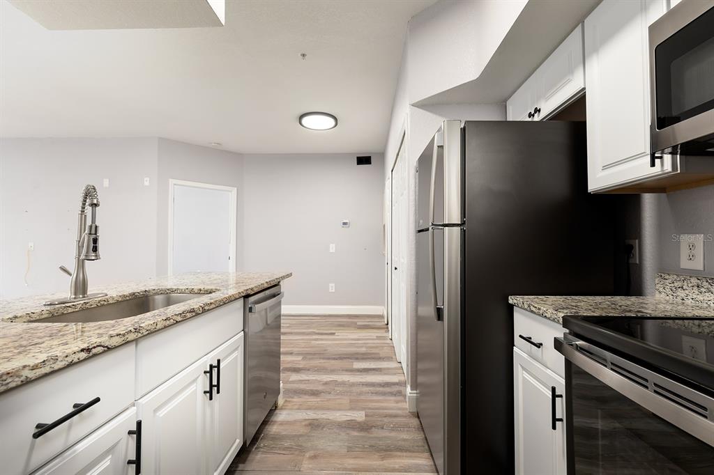A kitchen features white cabinets, granite countertops, stainless steel appliances, and wood-look flooring — 13015 PLANTATION PARK CIRCLE UNIT 1027, ORLANDO, FL