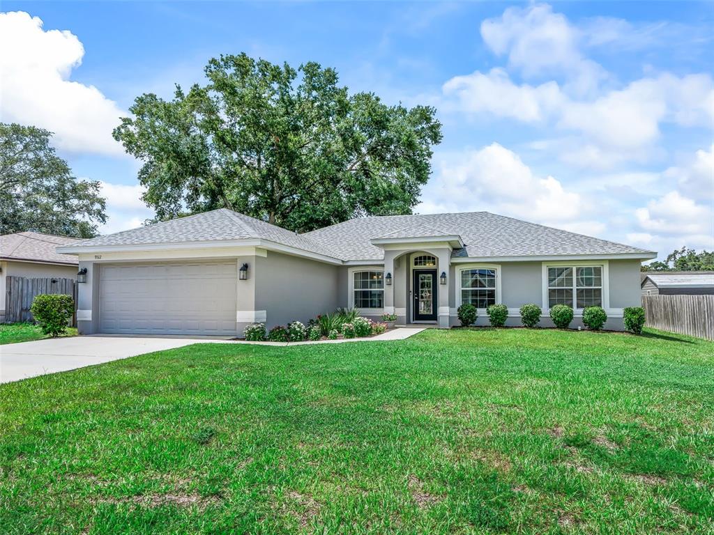 A single-story suburban house with a gray stucco exterior, a two-car garage, and a lawn — 9312 SE 162ND PLACE, SUMMERFIELD, FL