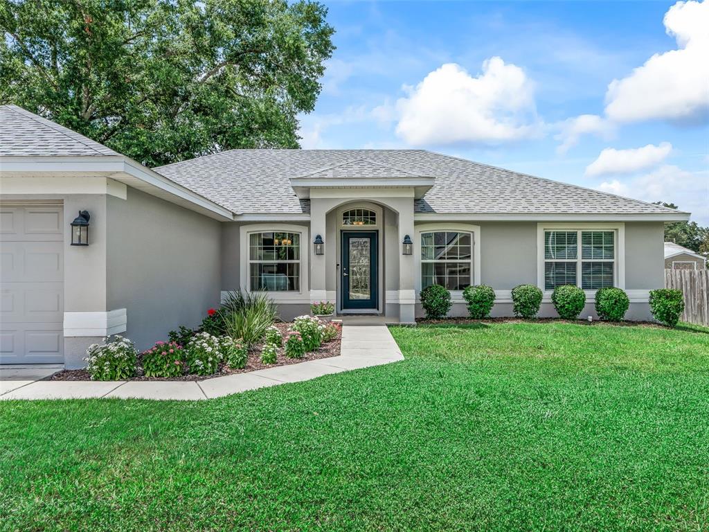 A gray single-story house with a dark front door, a concrete walkway, and manicured landscaping — 9312 SE 162ND PLACE, SUMMERFIELD, FL